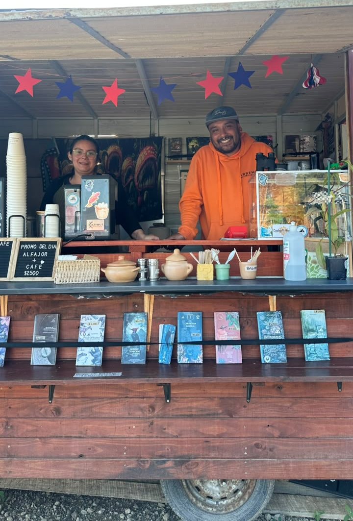 El equipo de ARREMO sonriendo en la ventana del quiosco, con la pizarra de la promo del día, pailas de greda y libros de naturaleza